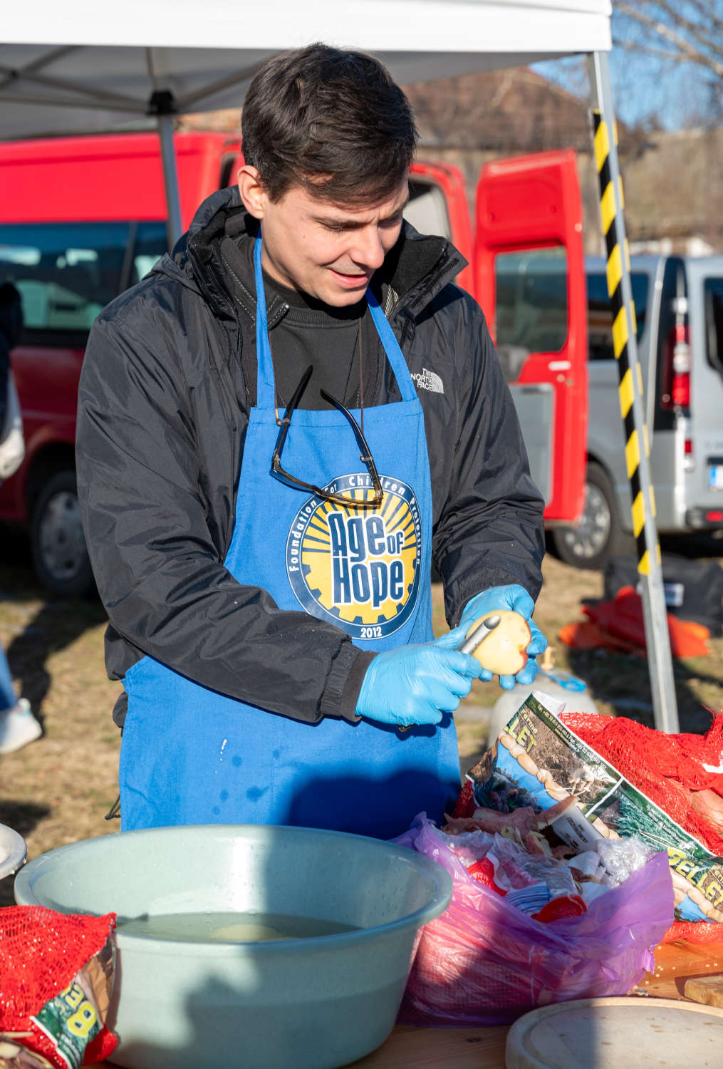 Önkéntes Age of Hope kötényében krumplit pucol a szabadtéri főzőállomáson