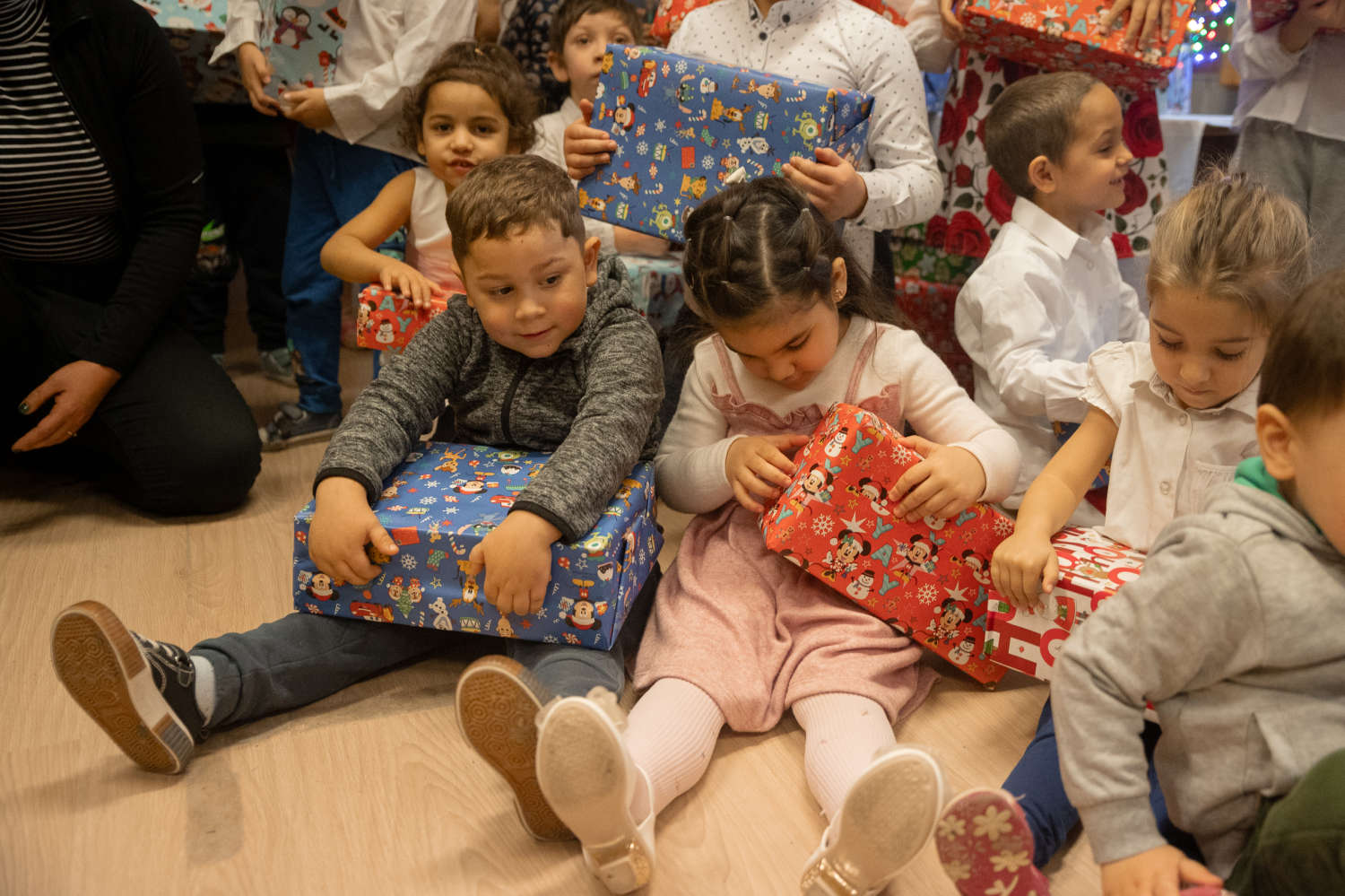 Gyerekek a földön ülve bontogatják a cipősdoboz-ajándékaikat