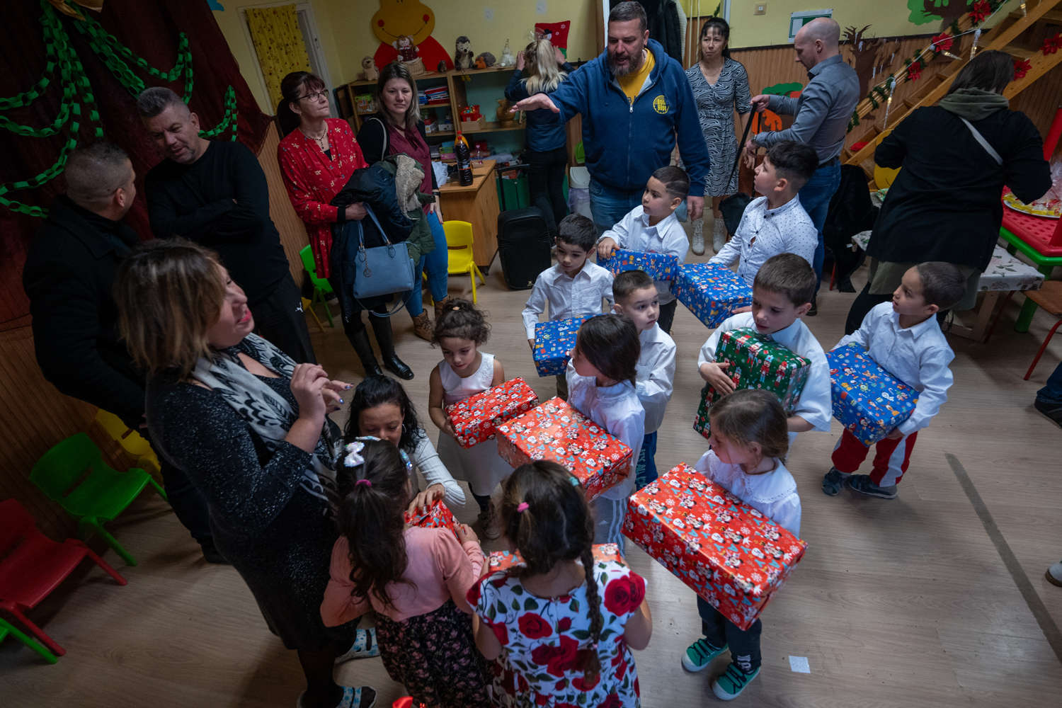 Önkéntesek ajándékokat osztanak óvodás gyerekeknek egy feldíszített teremben